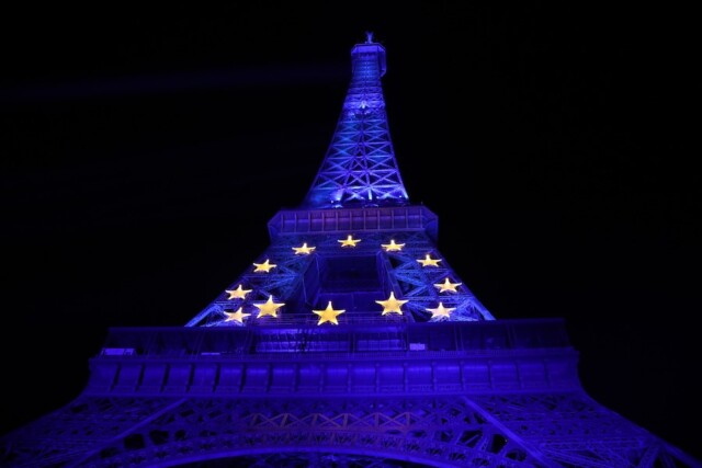 Nočna slika modro svetljenega Eifflovega stolpa, na katerem svetijo v krog postavljene rumene zvezdice