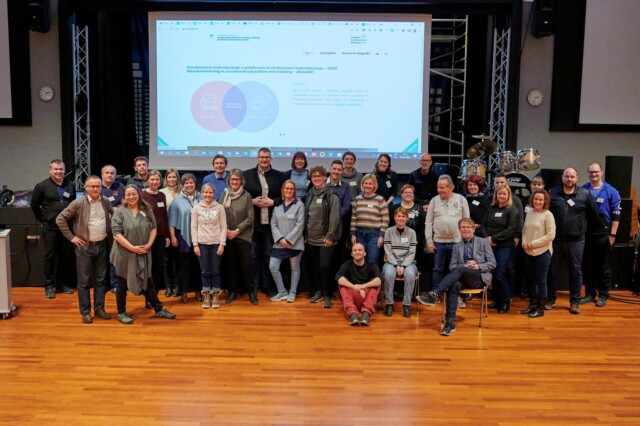Skupinska fotografija projektnih partnerjev v projektu KIPSI, študijski obisk na Norveškem (april 2022). Skupina nasmejanih ljudi - predstavnikov partnerskih organizacija. V ozadju je prosojnica z napisom Kombinirano izobraževanje v poklicnem in strokovnem izobraževanju-KIPSI / Blended learning in vocational education and tarining-BlendVET.