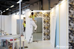 Prikaz tekmovanja v pleskanju; tekmovalka opravlja tekmovalno nalogo v lepljenju tapet in pleskanju stene.